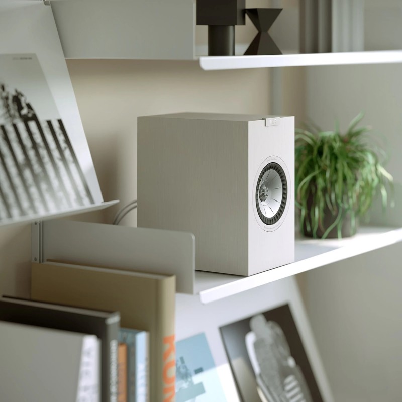 KEF Q1 Meta — altavoz blanco en una estantería con libros y plantas