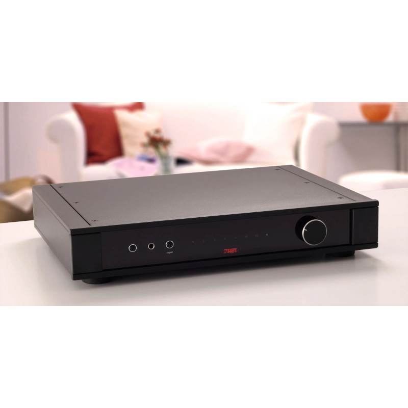 Rega Elex Mk4, sobre una mesa blanca en un salón, vista frontal con el logotipo rojo y el mando de volumen
