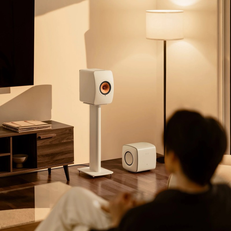 KEF KC62 Mineral White — en un salón junto a un altavoz sobre pie, ambiente